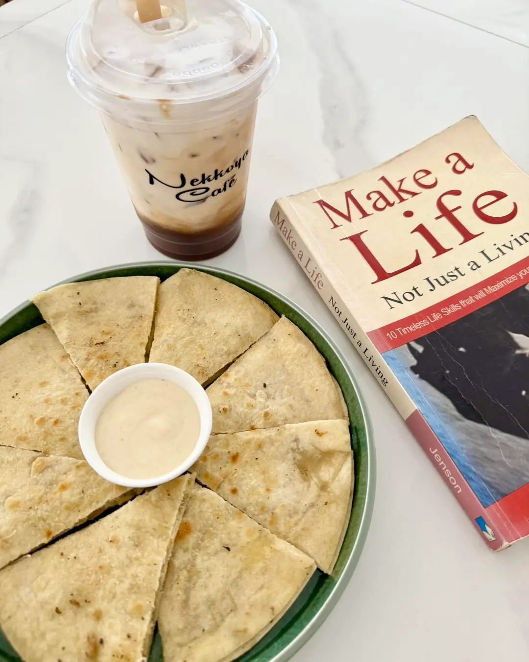 Iced coffee, a book and a plate of quesadillas on a white table