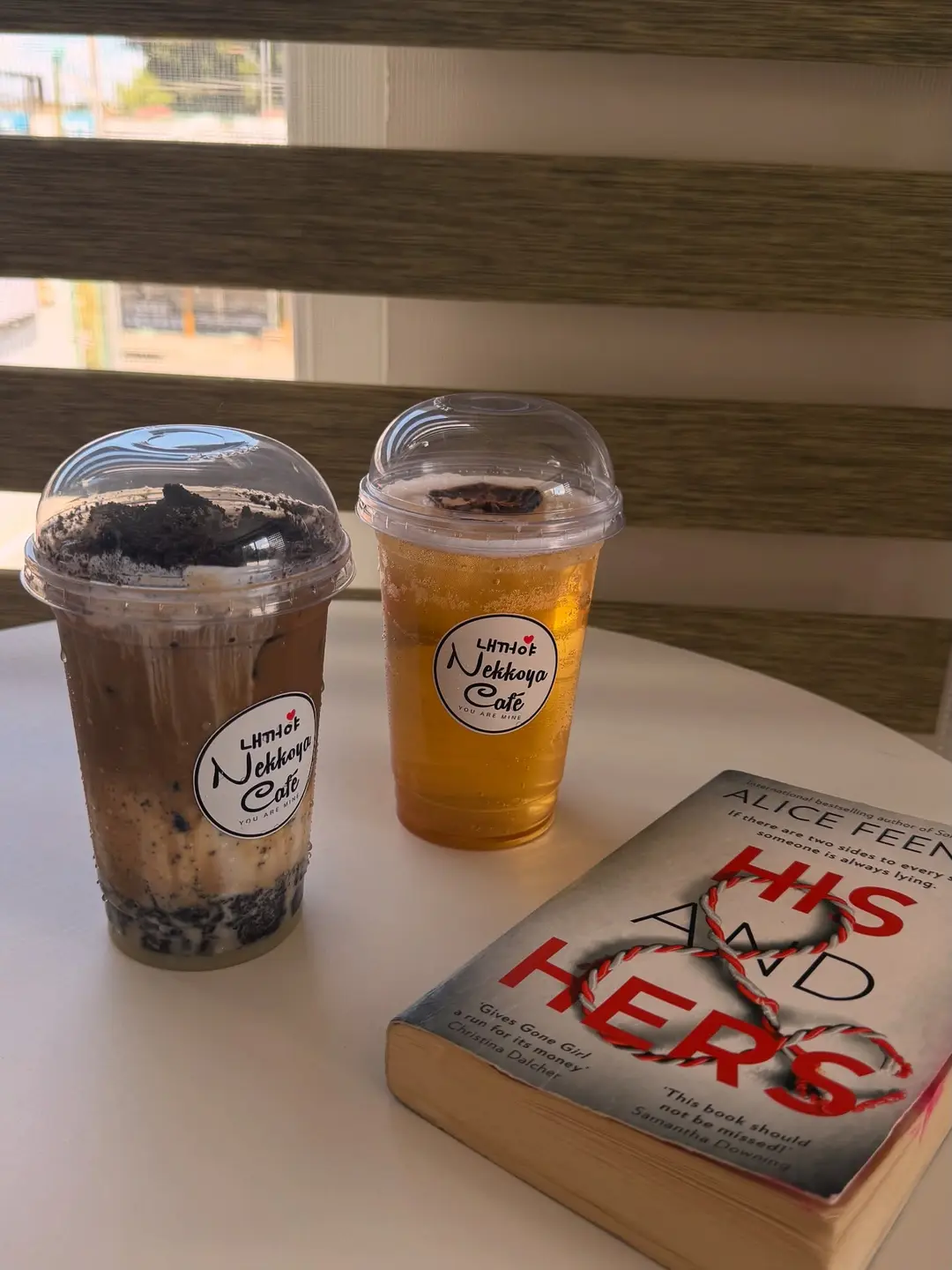 Two iced drinks beside a novel on the window ledge