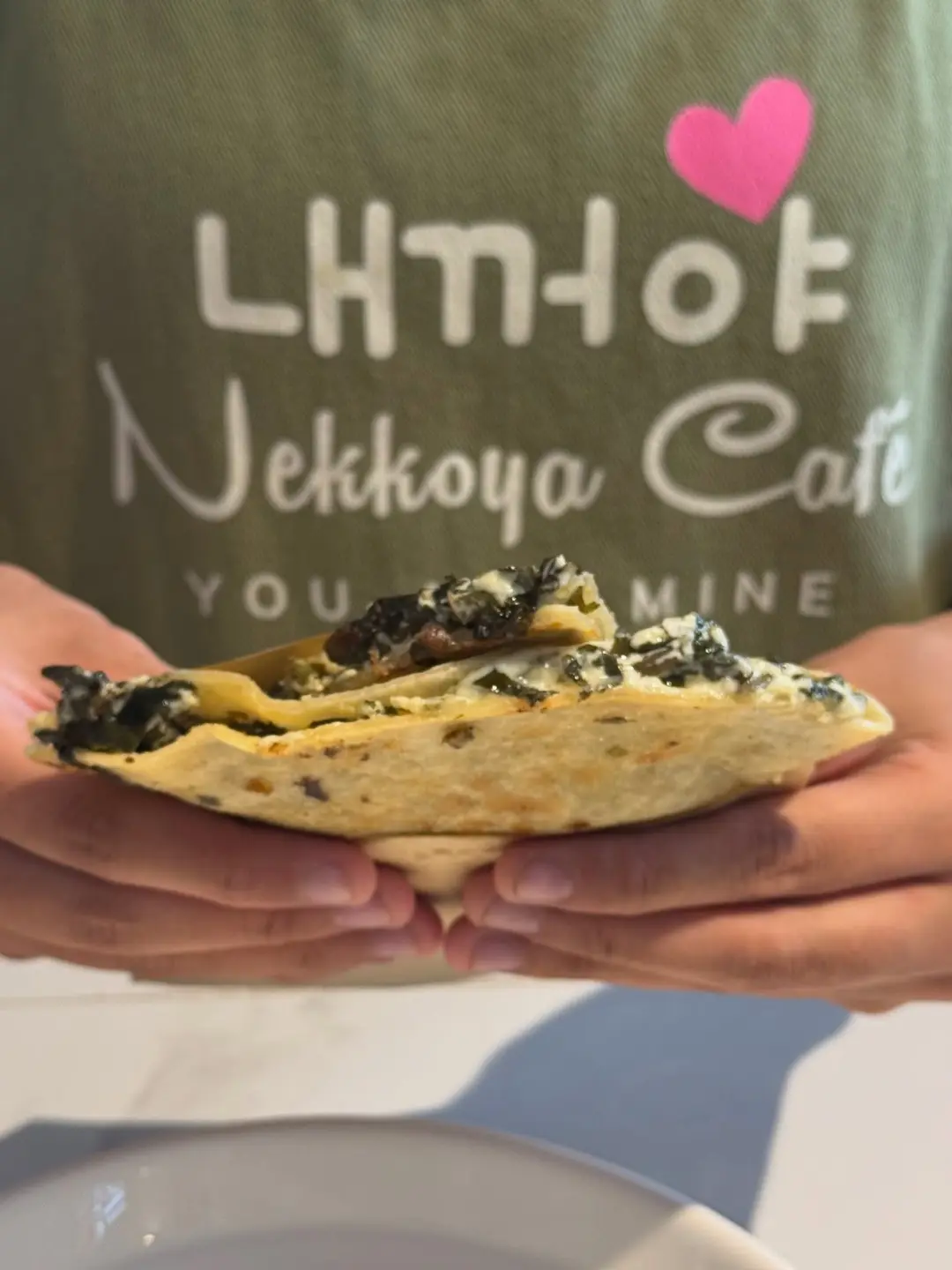 A croffle held up in front of a Nekkoya 내꺼야 shirt