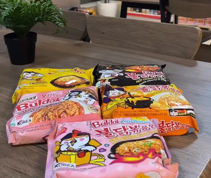 Samyang Buldak packets on a table with the ramyeon shelves behind