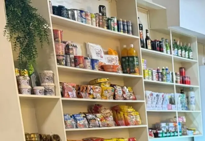 The 1F shelf wall stocked with ramyeon packets, snacks, drinks and gold bowls